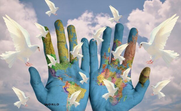 Manos con el mapa del mundo rodeadas de palomas que simbolizan la paz y la armonía