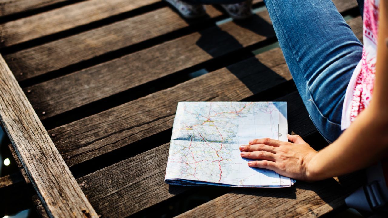 persona sentada sobre una superficie de madera oscura sostiene un mapa doblado en la mano