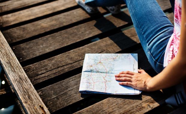 persona sentada sobre una superficie de madera oscura sostiene un mapa doblado en la mano