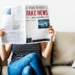 Persona sentada en un sofá sostiene un periódico en el que se lee "Fake News"