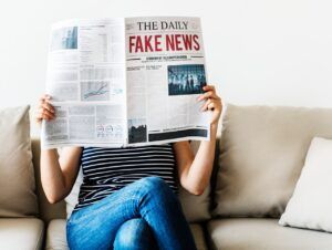 Persona sentada en un sofá sostiene un periódico en el que se lee "Fake News"