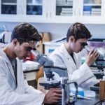 Laboratory research by two male scientists in laboratory using a microscope and laboratory glassware for scientific research