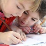 two little girl drawing with a pencil on a notebook