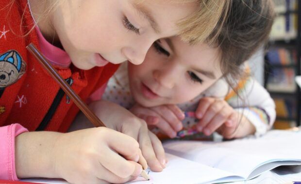 two little girl drawing with a pencil on a notebook