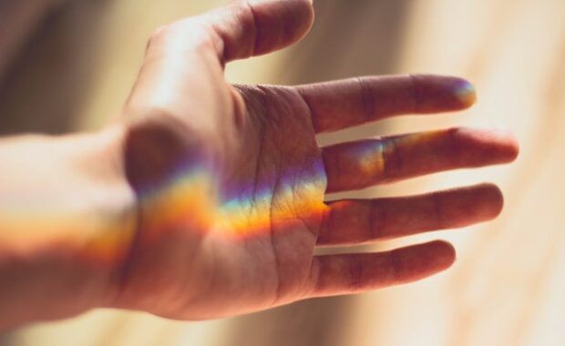 Mano tendida en son de paz con un reflejo de arcoiris en ella