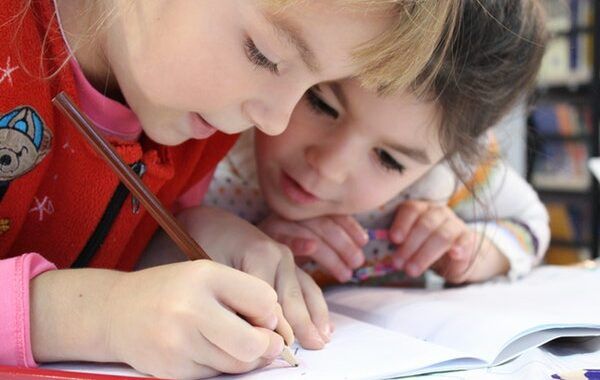 dos niñas pequeñas escriben concentradas en un cuaderno