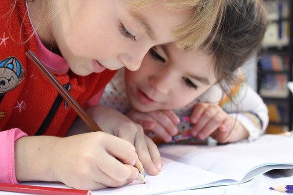 dos niñas pequeñas escriben concentradas en un cuaderno