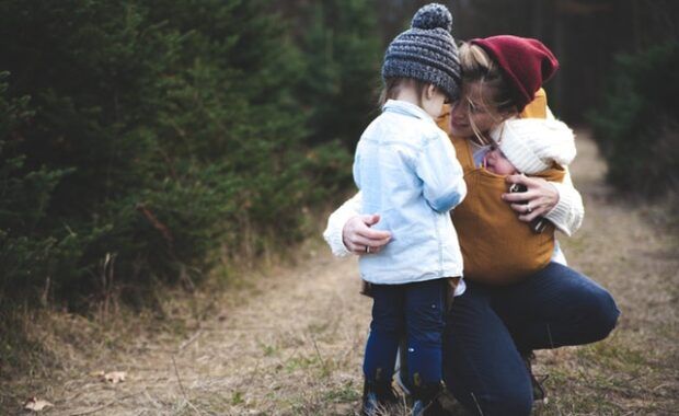 madre abrazando a su hijo pequeño mientras lleva a un bebé atado a sí misma