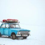 Coche viejo de color azul con un objeto atado sobre la vaca sobre un fondo cubierto de nieve