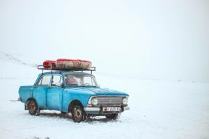 Coche viejo de color azul con un objeto atado sobre la vaca sobre un fondo cubierto de nieve