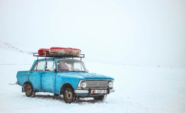 Coche viejo de color azul con un objeto atado sobre la vaca sobre un fondo cubierto de nieve