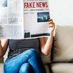 Persona sentada en un sofá sostiene un periódico en el que se lee "Fake News"