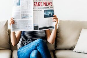 Persona sentada en un sofá sostiene un periódico en el que se lee "Fake News"