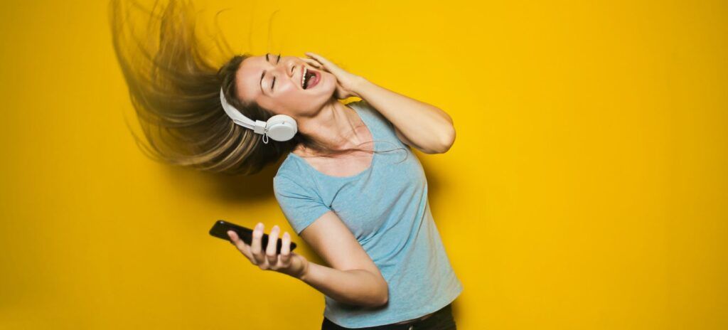 Blonde girl dancing with headphones and a mobile phone in her right hand