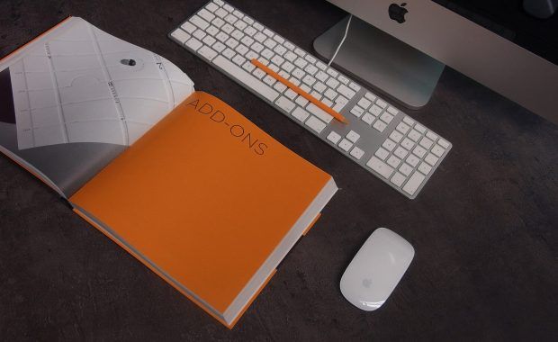 libreta naranja abierta junto a ordenador mac, sobre la mesa de un escritorio