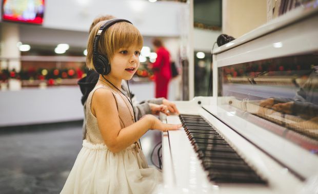 Una niña vestida de blanco toca un piano blanco en un centro comercial