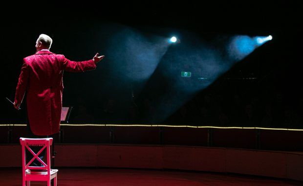 Vista de espaldas de un actor vestido de rojo que saluda hacia la oscuridad del patio de butacas