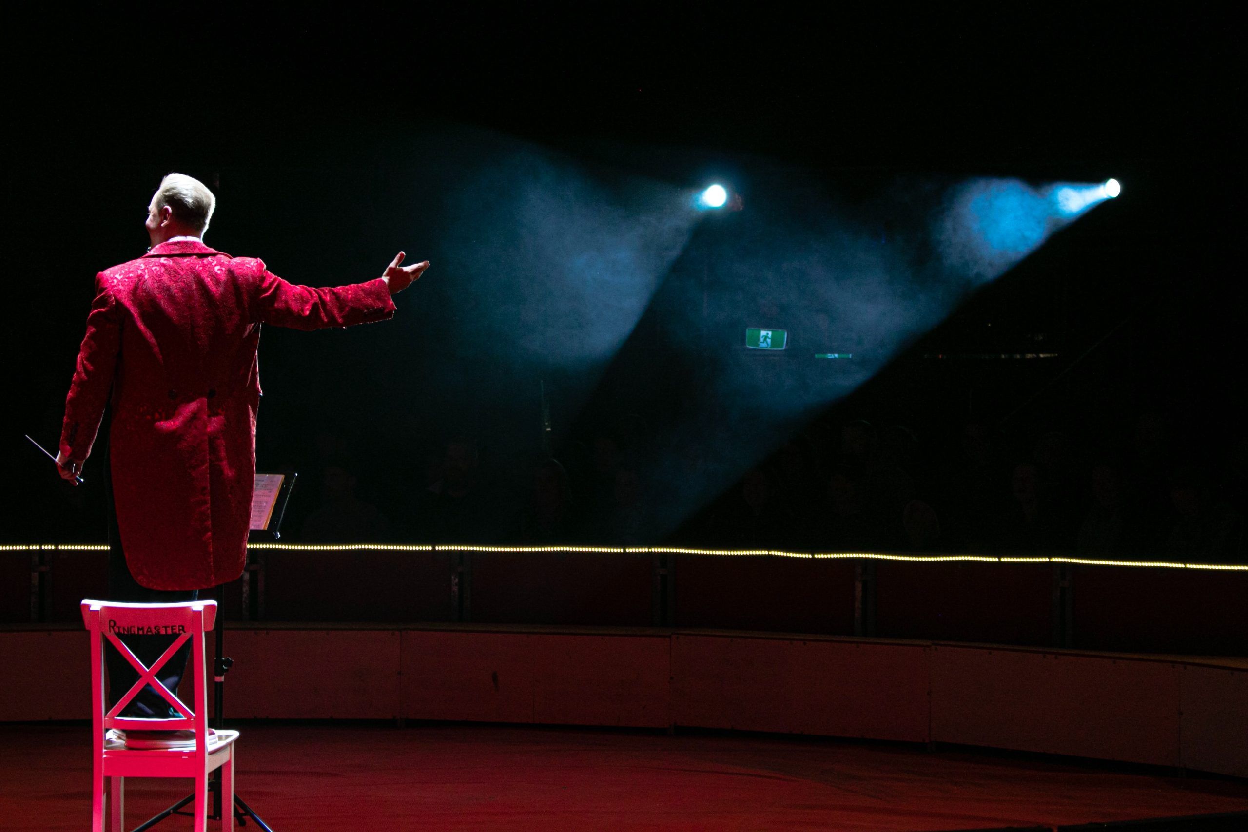 Vista de espaldas de un actor vestido de rojo que saluda hacia la oscuridad del patio de butacas