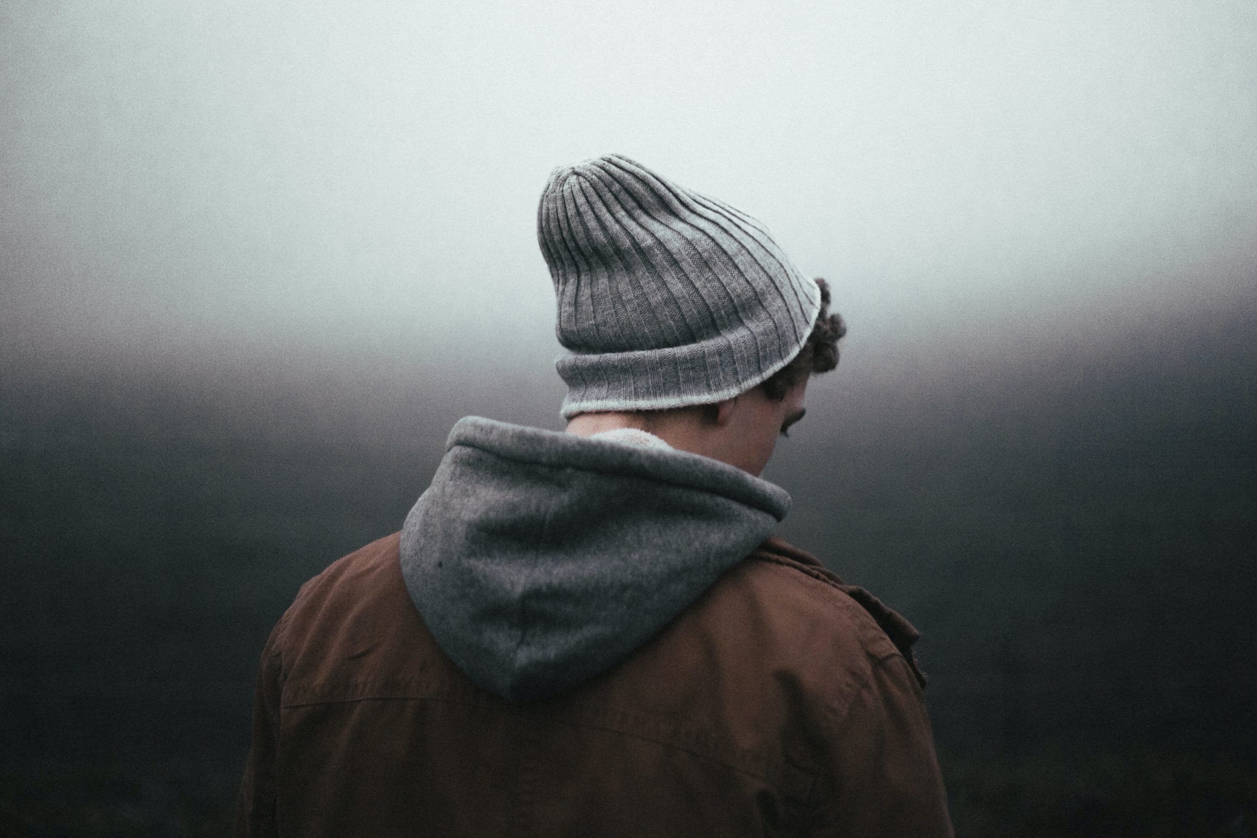 Primer plano de espaldas de un joven con ropa de invierno sobre un fondo gris oscuro