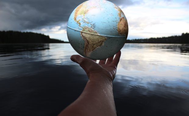 Una mano sostiene un modelo de un globo terráqueo frente a un cuerpo de agua