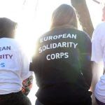 Mujeres sentadas de espaldas a la cámar con camisas en las que se lee "European Solidarity Corps"