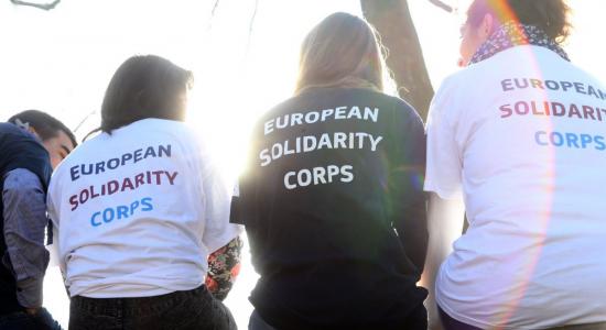 Mujeres sentadas de espaldas a la cámar con camisas en las que se lee "European Solidarity Corps"