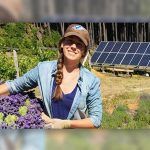 Granjera joven mira a cámara sonriendo y sosteniendo un cubo lleno de flores violetas