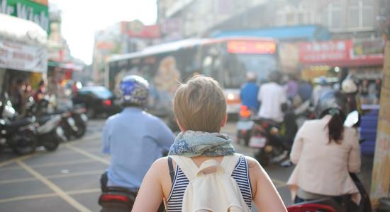 Vista trasera de una mujer con mochila que camina entre la multitud en un centro urbano