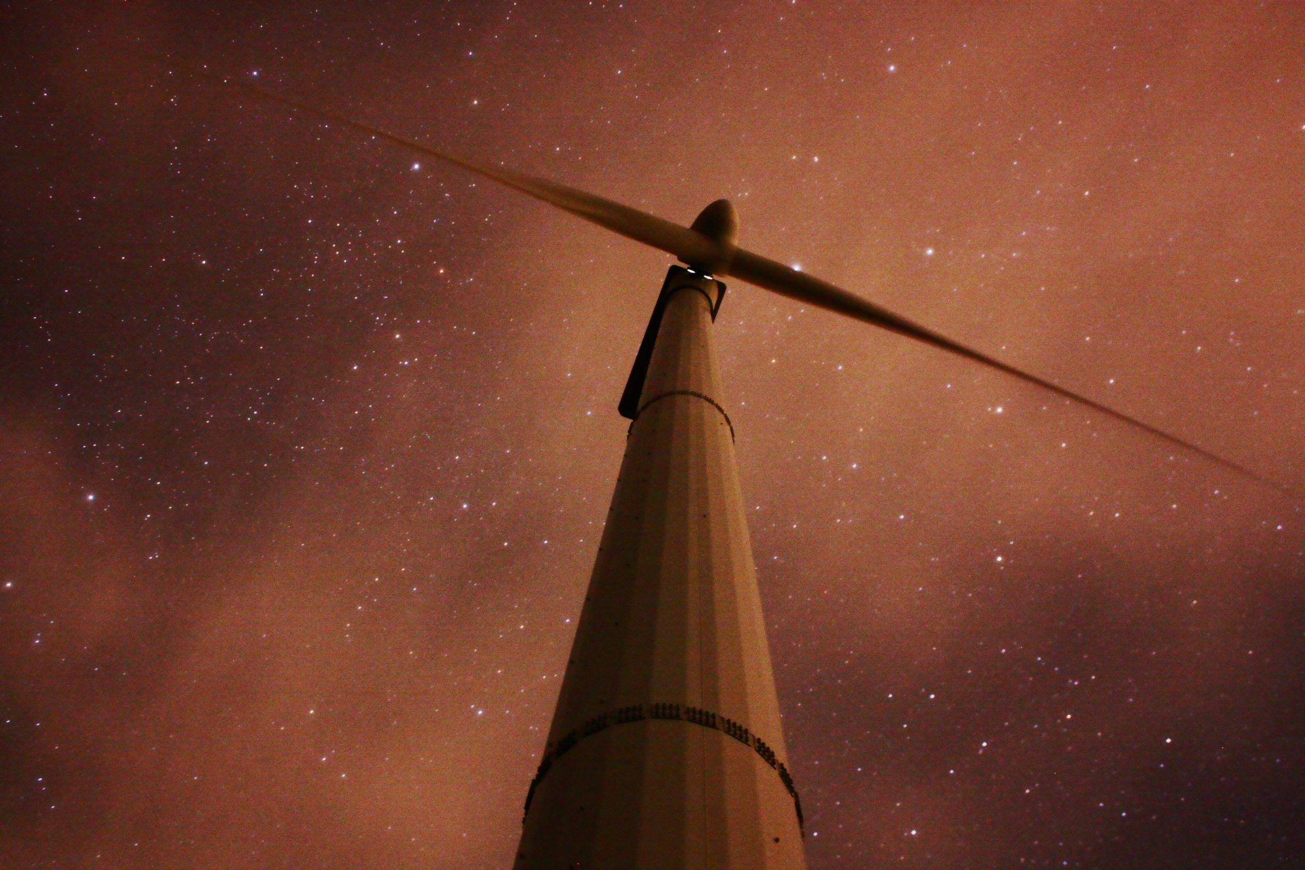 Turbina de energía eólica en contrapicado, con un cielo nocturno, estrellado y anaranjado de fondo
