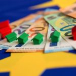 Billets de euro dispuestos en abanico sobre los que hay colocadas unas casitas rojas y verdes del juego de mesa Monopoly