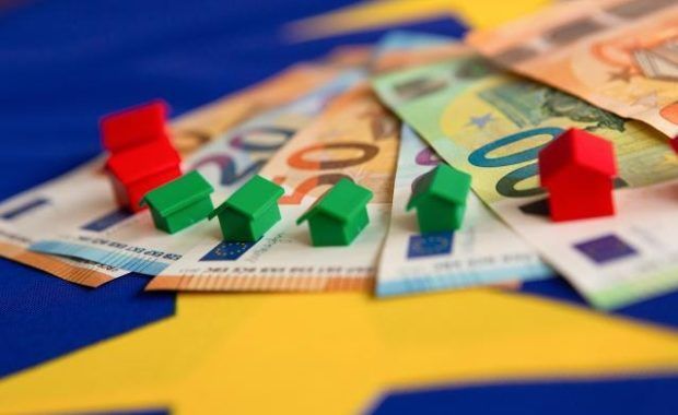 Billets de euro dispuestos en abanico sobre los que hay colocadas unas casitas rojas y verdes del juego de mesa Monopoly