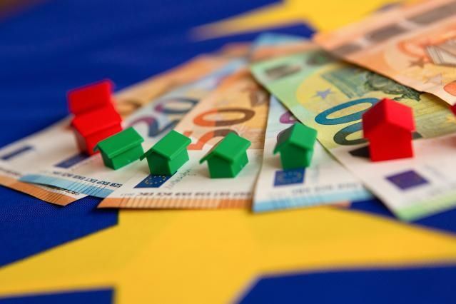 Billets de euro dispuestos en abanico sobre los que hay colocadas unas casitas rojas y verdes del juego de mesa Monopoly