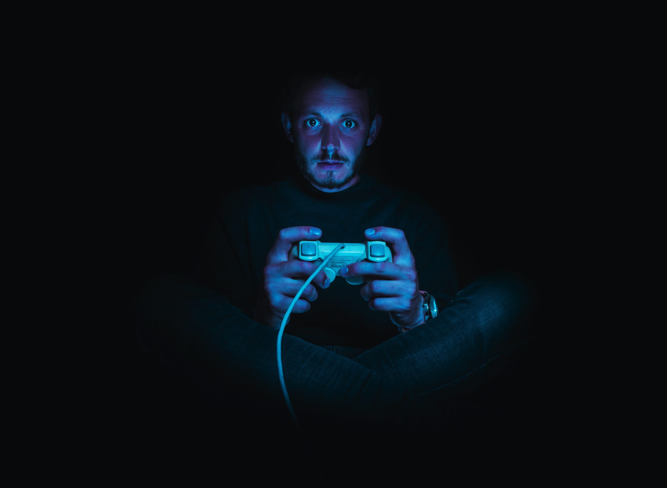 Plano frontal de un hombre con un mando de consola que juega en la oscuridad