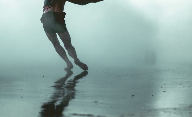 Figura humana caminando sobre una superficie acuosa y un fondo neblinoso