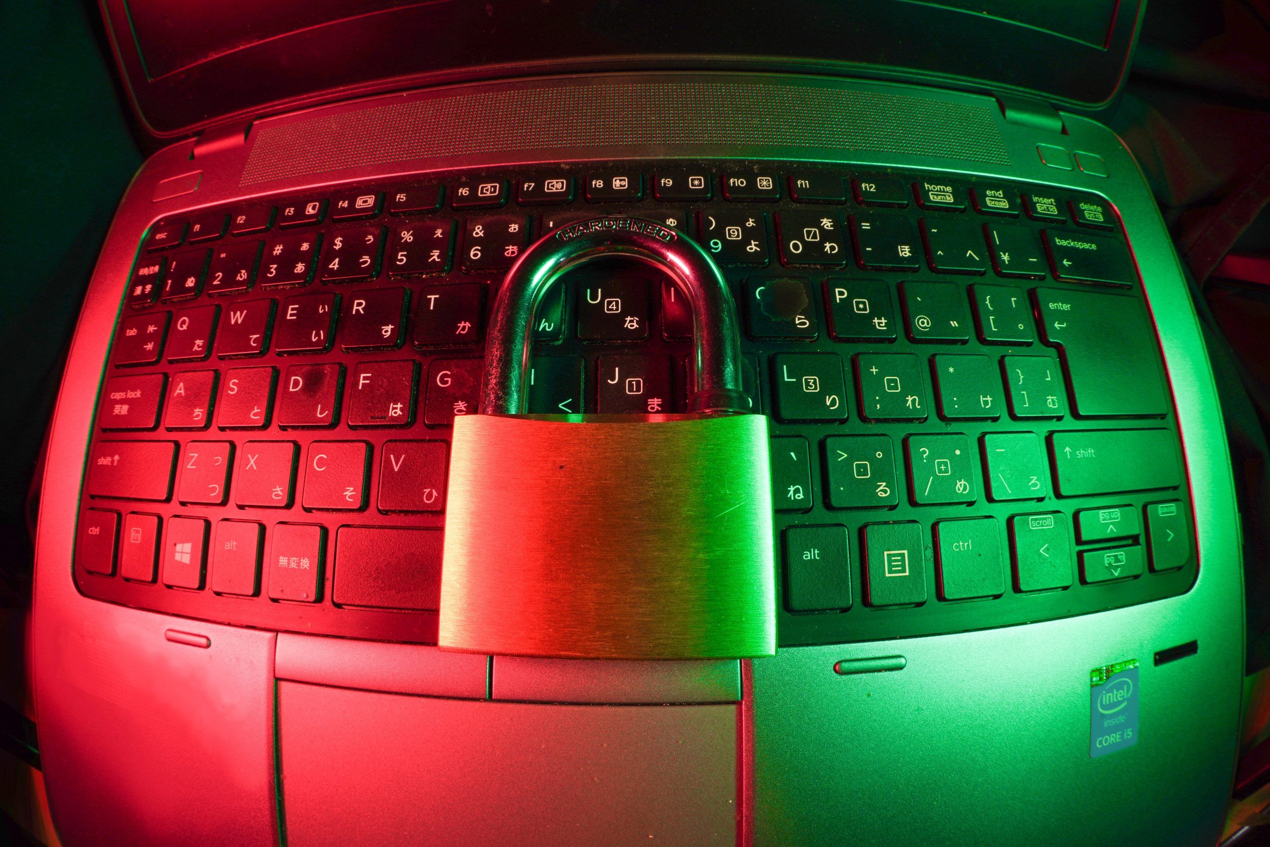 Un candado reposa sobre un teclado de un ordenador portátil. La imagen está enfocada con un ojo de pez e iluminada con luz roja y verde