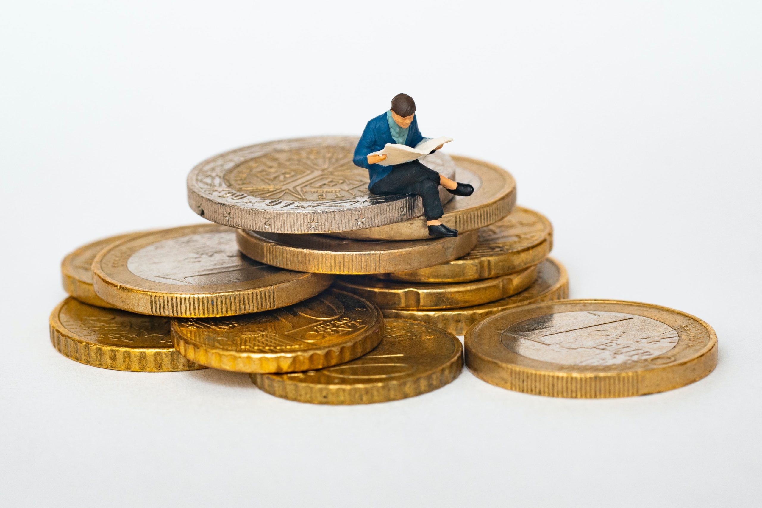 Miniatura de un hombre leyendo el periódico sentado sobre un montón de monedas de 1 y 2 euros