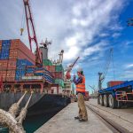 vista trabajador en un puerto y un barco de carga