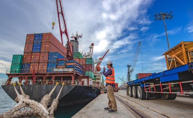 vista trabajador en un puerto y un barco de carga