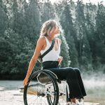 Una joven rubia mira al horizonte sentada en una silla de ruedas en medio de un bosque