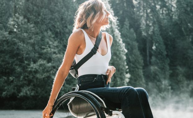 Una joven rubia mira al horizonte sentada en una silla de ruedas en medio de un bosque