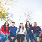 Grupo de jóvenes, sentados en un banco, sornríen a cámara