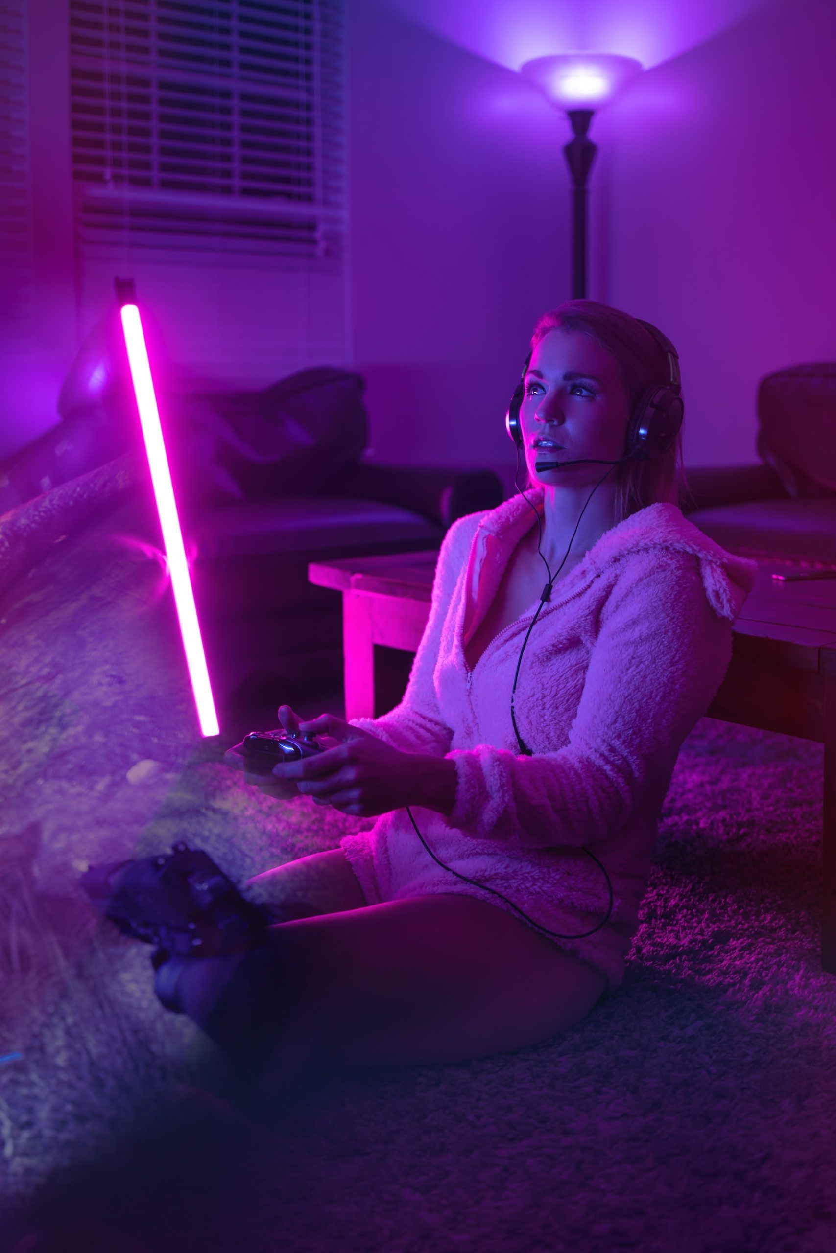Jugadora de videjuegos sentada en el suelo en una habitación iluminada por luz de neón rosa