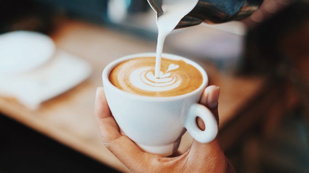 persona sirviendo leche a un café