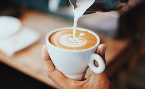 persona sirviendo leche a un café