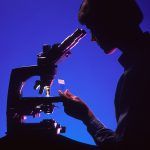 Silueta a contraluz de una persona de perfil observando por un microscopio