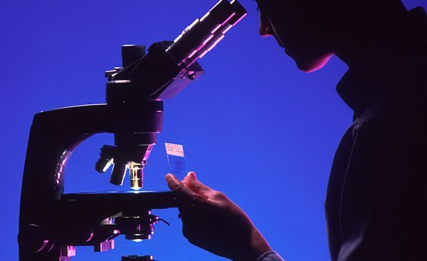 Silueta a contraluz de una persona de perfil observando por un microscopio
