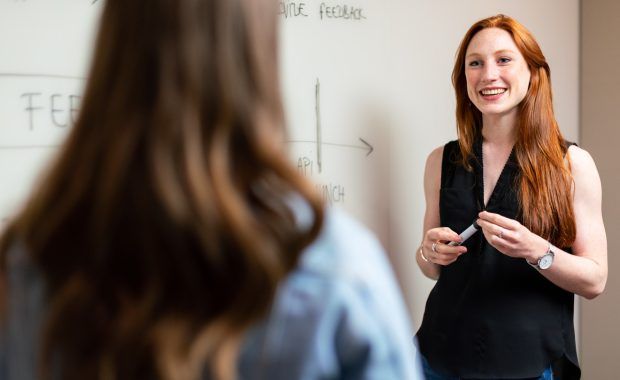 profesora junto a una pizarra hablando con una alumna